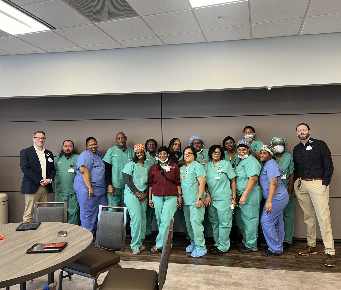 Group of diverse healthcare workers in green scrubs gathered together in an office conference room.