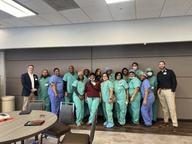 Group of diverse healthcare workers in green scrubs gathered together in an office conference room.