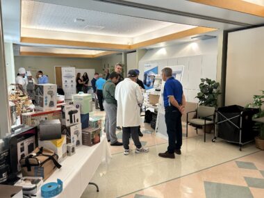 A trade show booth displaying healthcare products, with attendees browsing and interacting with representatives.