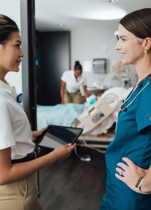 Nurse and doctor smiling at each other in hospital hallway, representing compassionate healthcare teamwork