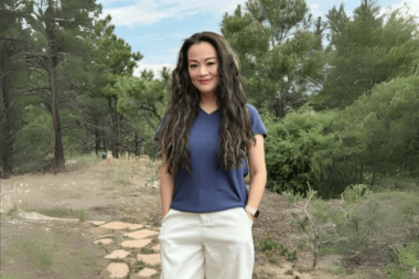Smiling woman with long wavy hair standing on a path in a lush green forest