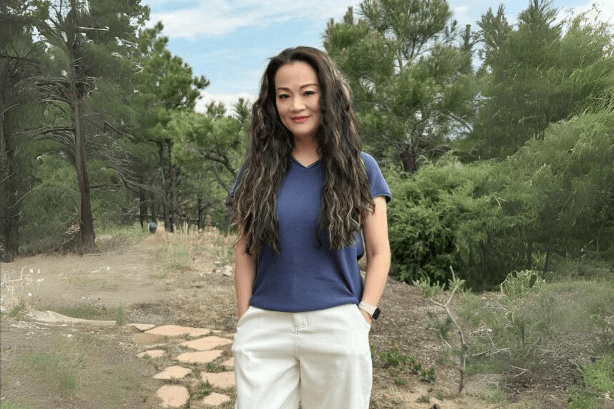 Smiling woman with long wavy hair standing on a path in a lush green forest