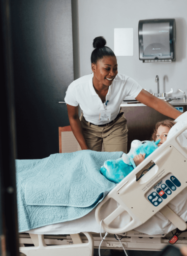 Smiling nurse adjusting baby in hospital bassinet as colleagues converse, healthcare support services