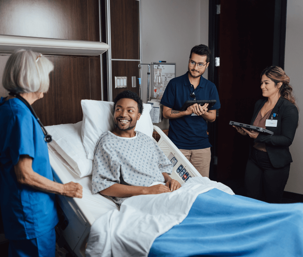 Patient smiling in hospital bed with healthcare team discussing treatment plan on digital tablet