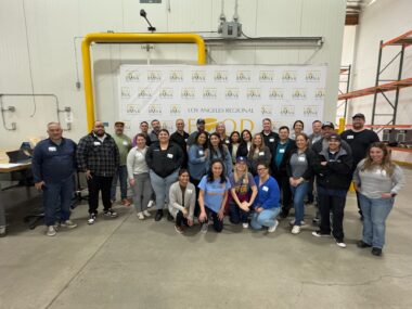 A group of volunteers poses at the Los Angeles Regional Food Bank, smiling in a warehouse setting with the food bank's logo in the background.